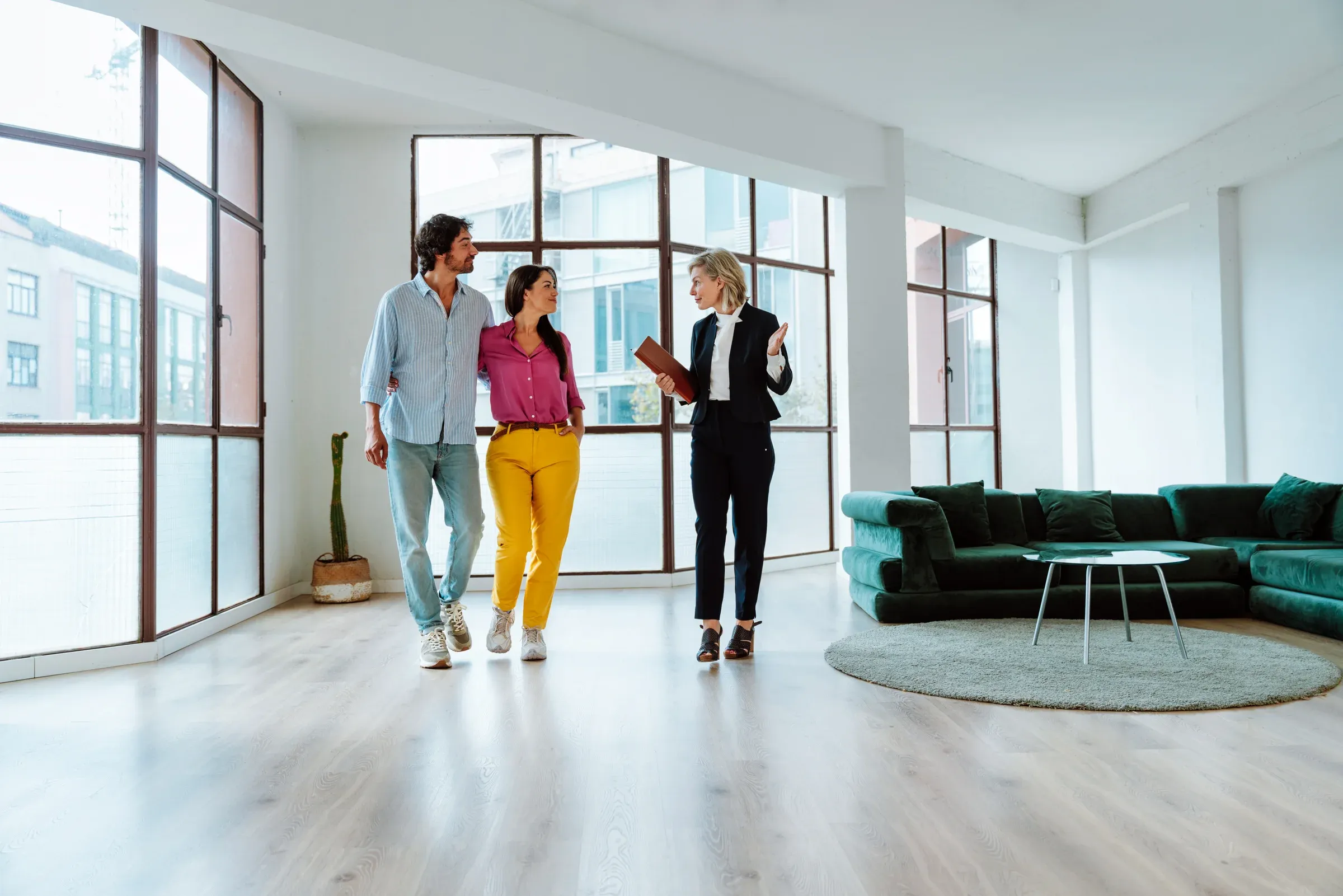 Zwei Interessenten besichtigen mit einer Begleiterin eine helle Wohnung mit hohen Fenstern