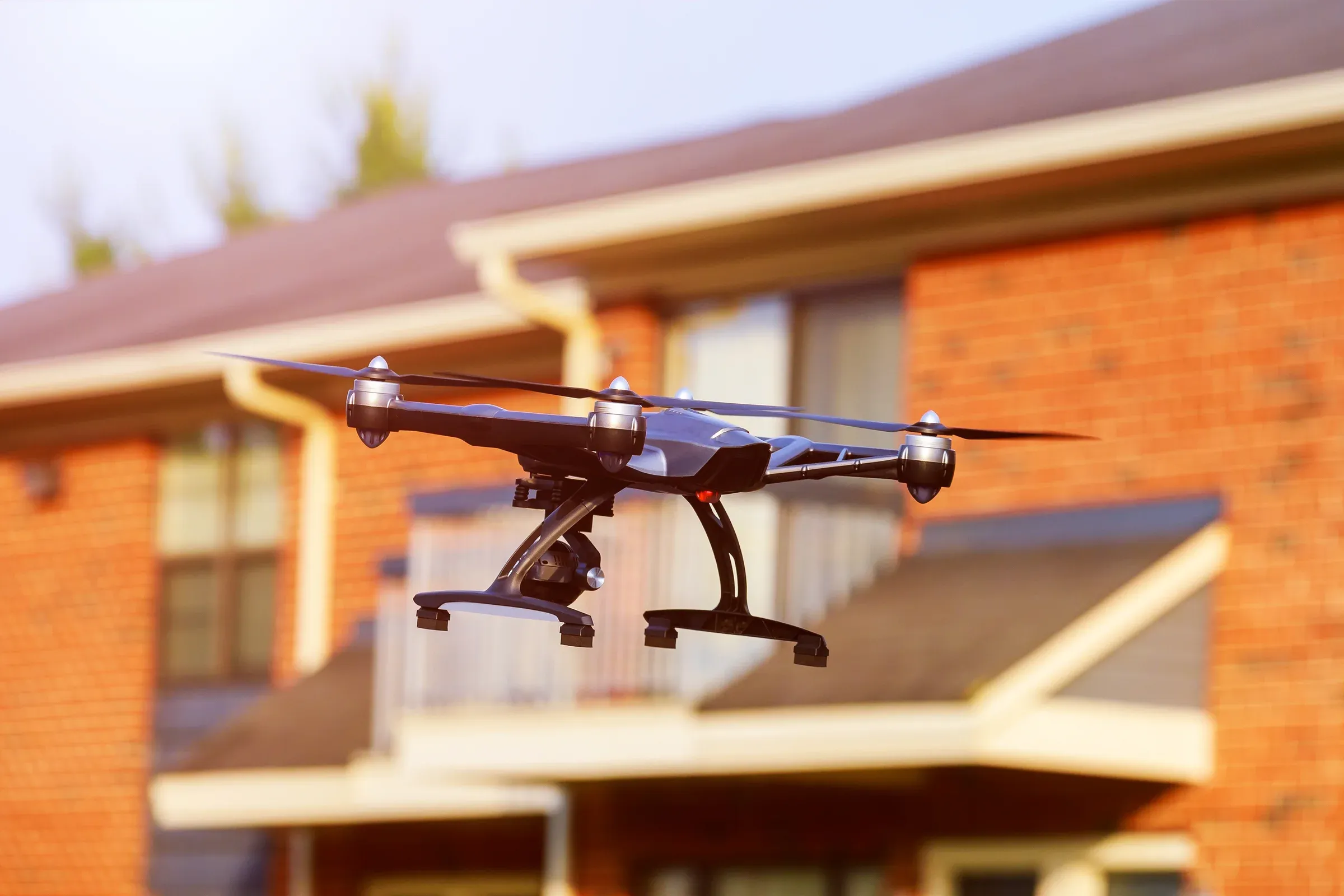 Drohne mit Kamera fliegt vor einem Wohnhaus mit Ziegeldach