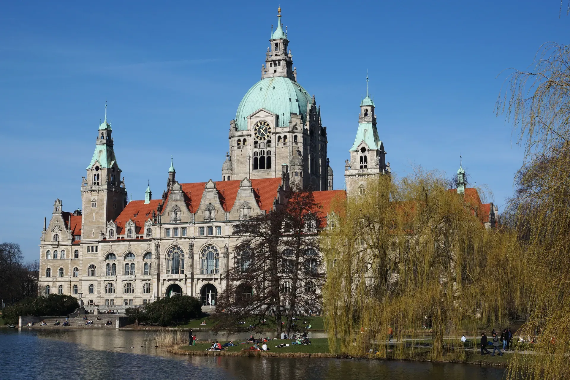 Das Neue Rathaus in Hannover mit grüner Kuppel hinter einem Teich und Bäumen